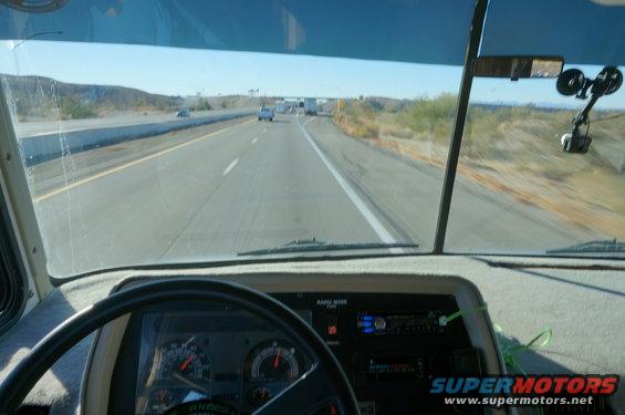 View from inside a vehicle's cab, looking out the windshield at a highway. Dashboard and steering wheel visible