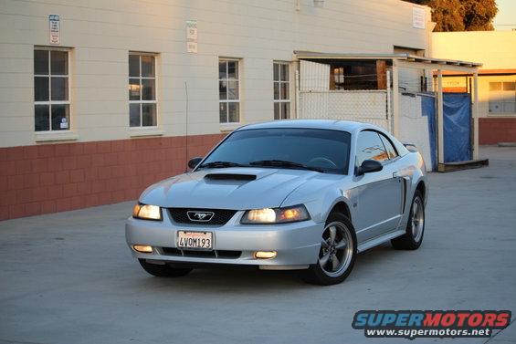 Silver 2002 Ford Mustang coupe parked on concrete, front 3/4 view. Hood scoop and aftermarket wheels are visible