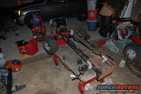 Rusty vehicle frame on a creeper cart with tools.