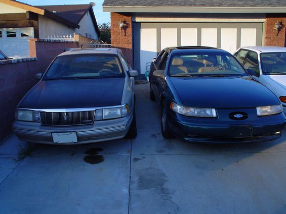 Dark blue Ford Taurus and a silver Lincoln Town Car parked in front of a garage