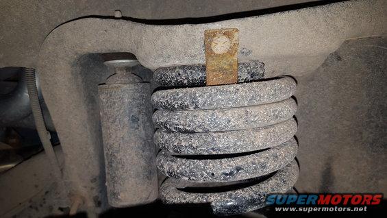 Rusty metal bracket on top of a dirty coil spring and shock absorber