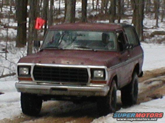 Maroon Ford Bronco driving on a snowy dirt road with trees in the background