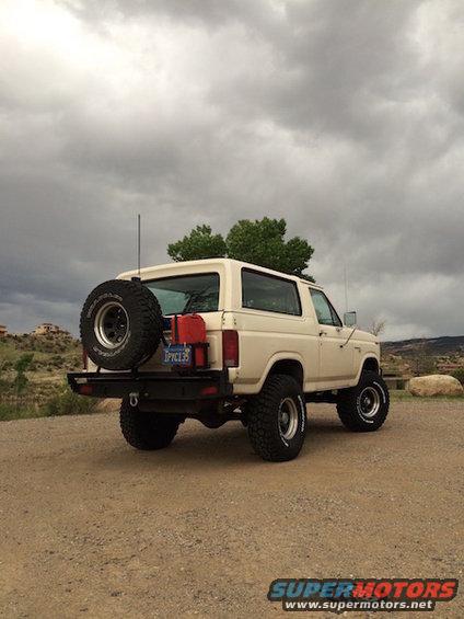 tan Ford Bronco with spare tire on back, red gas cans, and lifted suspension parked on dirt