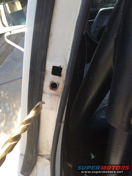 White door jamb with rust around a hole and a square cutout, a drill bit in the foreground