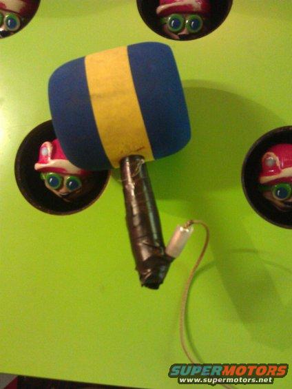 Whack-a-mole mallet with blue and yellow foam head, taped handle, and wire, against a green background with mole heads popping out