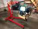 1979 Ford Bronco - Engine hoist lifting a blue engine assembly in a garage setting with a snowmobile in the background.