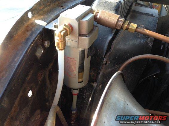 Air filter assembly with brass fittings and white tubing mounted on rusted metal