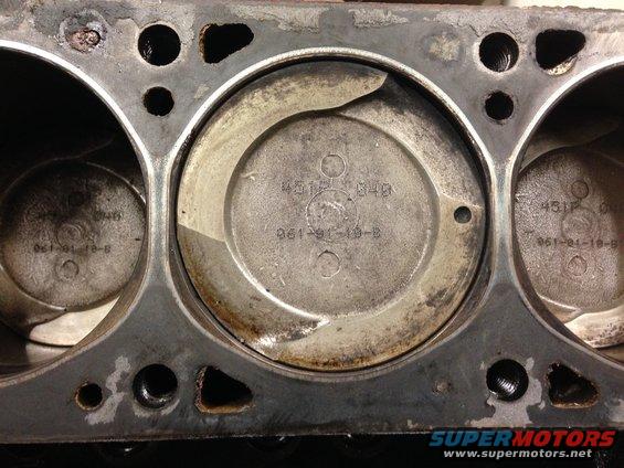 Close-up of an engine block showing three cylinders with pistons inside. Markings are visible on the pistons