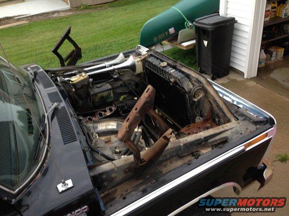 Engine bay of a black vehicle with hood open, showing engine components and aftermarket air horns