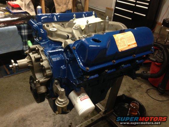 Blue V8 engine on stand with oil filter and fuel pump. Label on valve cover is visible