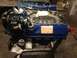 1979 Ford Bronco - Engine rebuild with a blue Ford V8 motor on a stand, an oil filter and various hoses.
