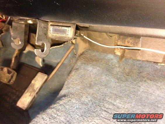 Vehicle interior showing pedals, carpet, and a small rectangular control panel
