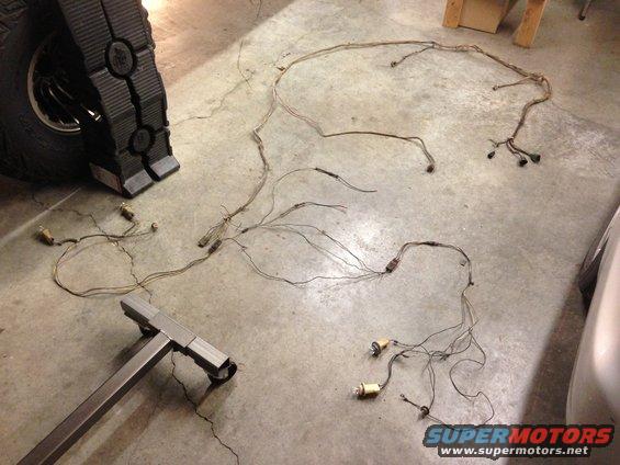 Vehicle wiring harness spread out on concrete floor next to a tire and jack stand