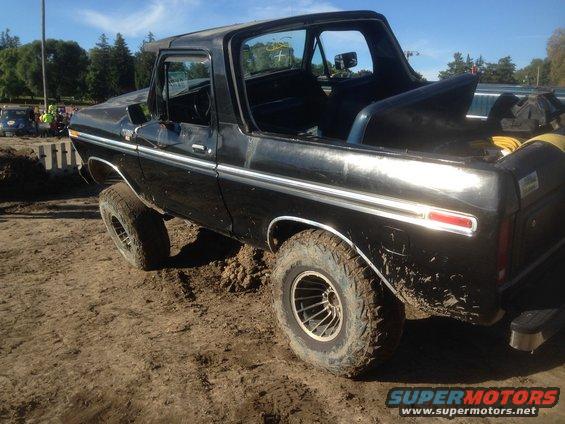 Black SUV with off-road tires stuck in mud, driver's door open