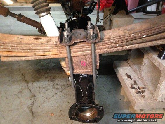 Leaf springs attached to a rear axle housing with U-bolts and nuts. Shock absorber visible above