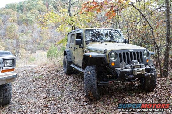 Ford Bronco front corner, tan Jeep Wrangler 3/4 front view, off-road tires, winch, wooded area