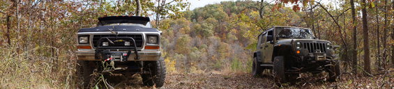 1979 Ford Bronco and Jeep Wrangler on a dirt path in autumn woods