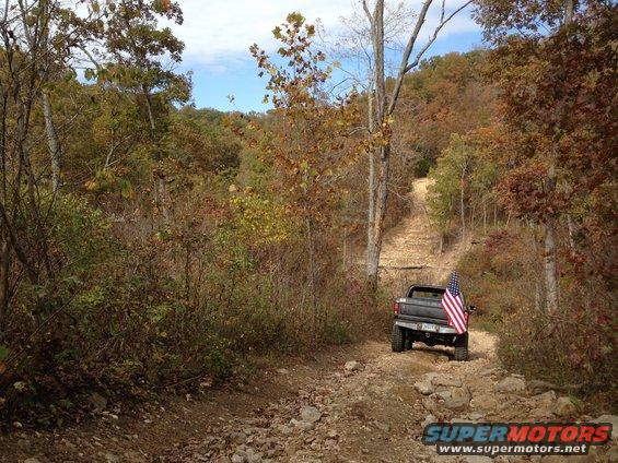 Pickup truck with American flag driving up a rocky dirt trail in autumn woods