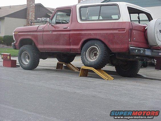 Red 1978 Ford Bronco with white top, lifted on yellow ramps. Toolbox nearby