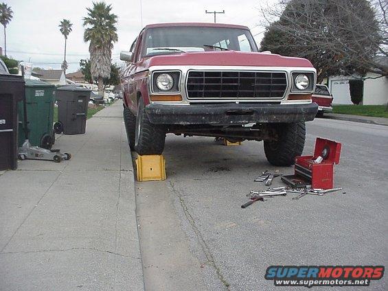 Red 1978 Ford Bronco on yellow blocks, front view, with tools on the street