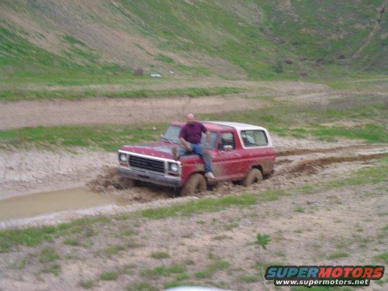 Red 1978 Ford Bronco stuck in mud with a man sitting on the hood