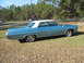 1972 Ford Ranchero - A vintage blue sedan with a white vinyl roof sits on a grassy field under a clear sky.