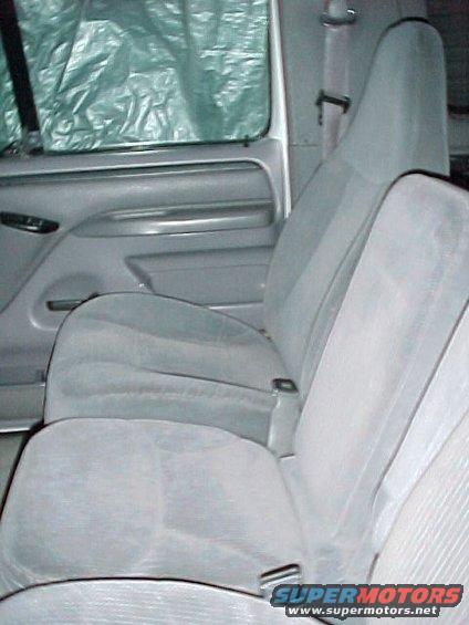 Gray cloth seats and door panel inside a vehicle. Window is covered with a tarp