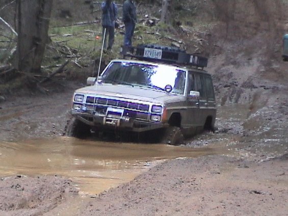 Jeep Cherokee XJ driving through a mud pit with people watching