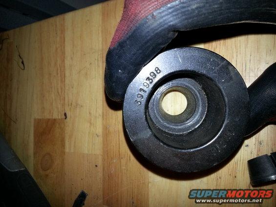 Metal part with numbers 3919398 stamped on it, held by a gloved hand over a wooden surface