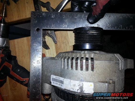 Alternator with a pulley being measured by a square ruler and a drill in the background