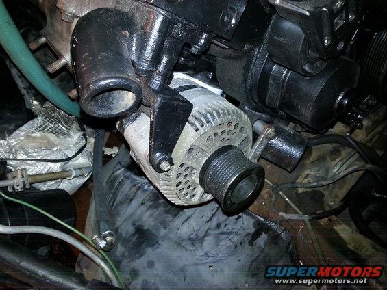 Close-up of vehicle alternator and black engine parts. Green hose visible
