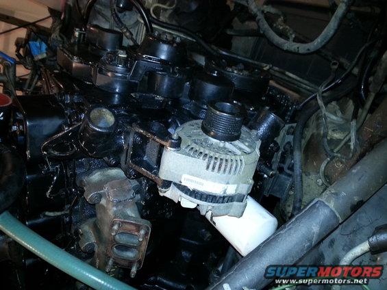 Engine bay with black engine block, alternator, and oil filter. Some hoses and wiring are visible