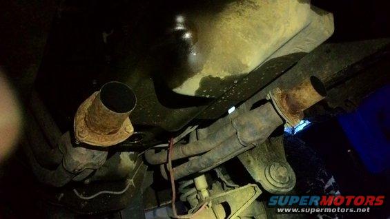 Underside of a vehicle showing rusty exhaust pipes and catalytic converter