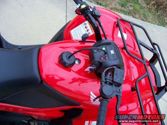 Close-up of a red ATV's handlebars, seat, and fuel tank. Has a black rack on the back