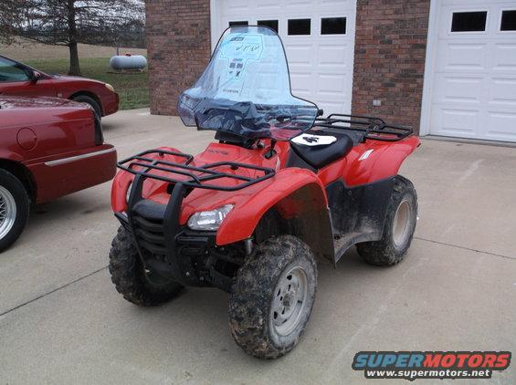 Red ATV with windshield, front view. Another red car is partially visible