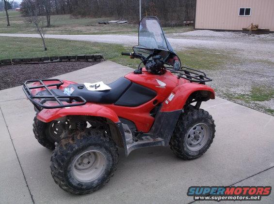 Red Honda ATV with a windshield and racks on front and back. A paper is on the seat