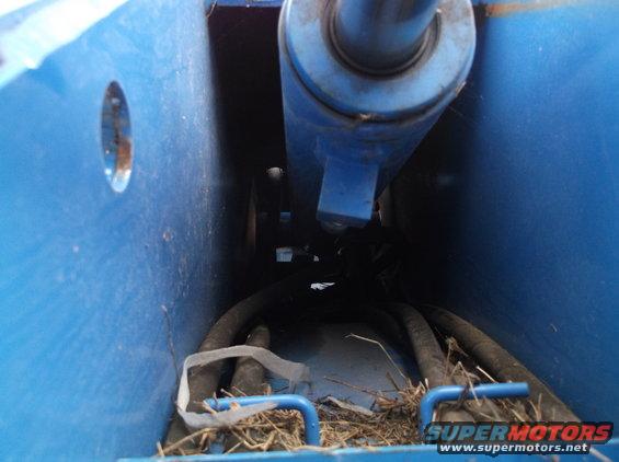 Blue hydraulic cylinder and hoses within a blue frame, with debris