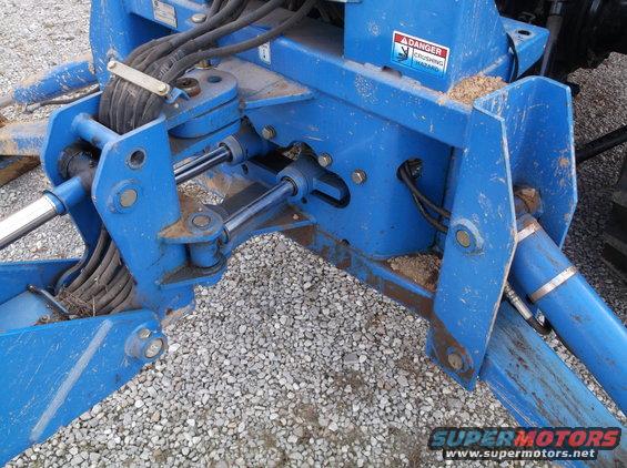 Close-up of a blue hydraulic attachment with hoses and cylinders, possibly for a tractor or backhoe