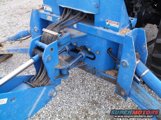 Blue hydraulic attachment with hoses and cylinders. Has danger labels
