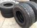 1986 Ford Bronco - Four Bridgestone Dueler tires are stacked on a concrete surface, with a vehicle frame visible behind them.