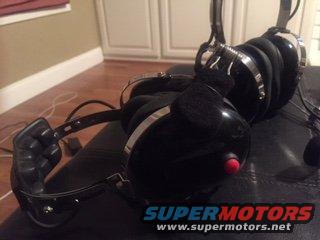 Several black aviation headsets with red buttons and coiled cords on a dark surface