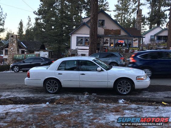 White sedan with chrome wheels parked on a snowy street, side view