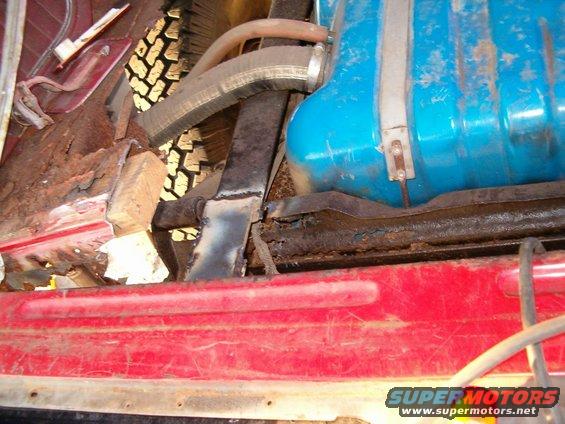 Interior shot of a vehicle showing significant rust damage, a blue fuel tank, and a spare tire