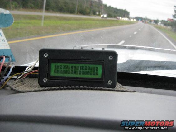 Custom digital display on dashboard showing numbers and text, with highway visible through windshield