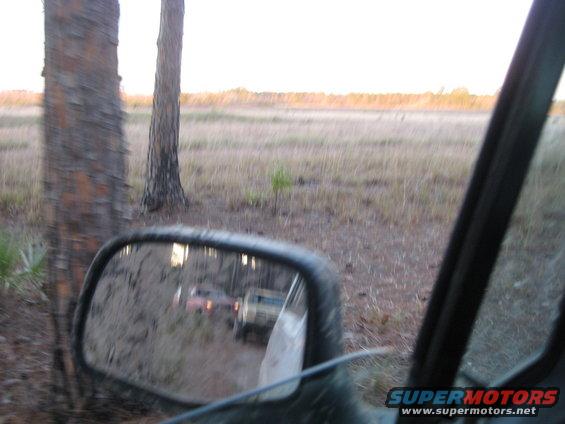 Two SUVs on dirt road reflected in side mirror