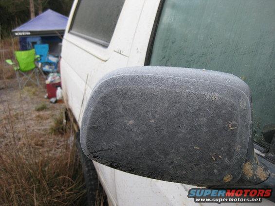 Frost covers the side mirror and part of the windshield of a white vehicle parked outdoors