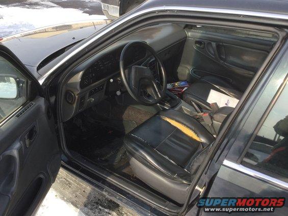 Black car interior with torn driver's seat, dashboard, and center console visible