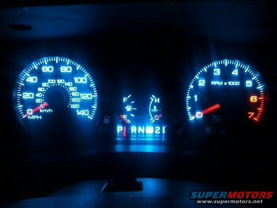 Car dashboard with glowing blue gauges, showing speed, RPM, fuel, and temperature