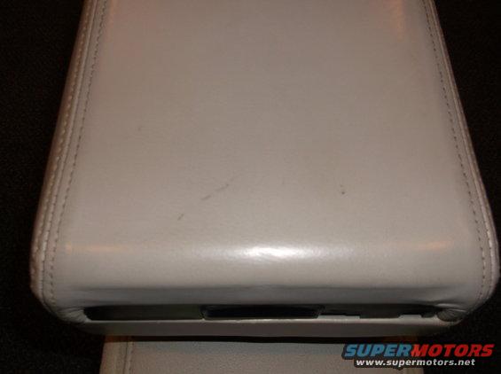 Light-colored leather center console lid with visible stitching and a dark slot at the bottom