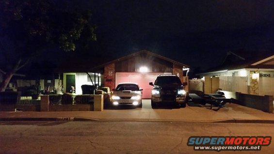 White coupe and black SUV parked in driveway at night